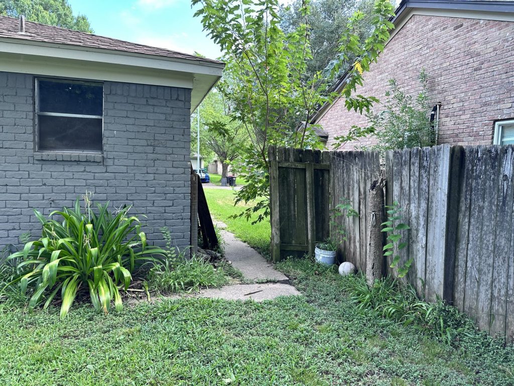 Overgrown side yard and aging fence of abandoned home bought for cash in Baytown TX