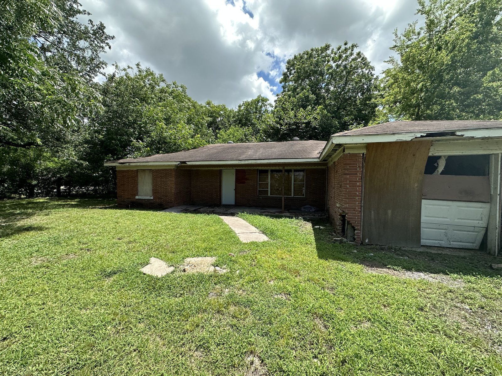 Front of abandoned brick home with boarded windows bought for cash as-is in Baytown TX