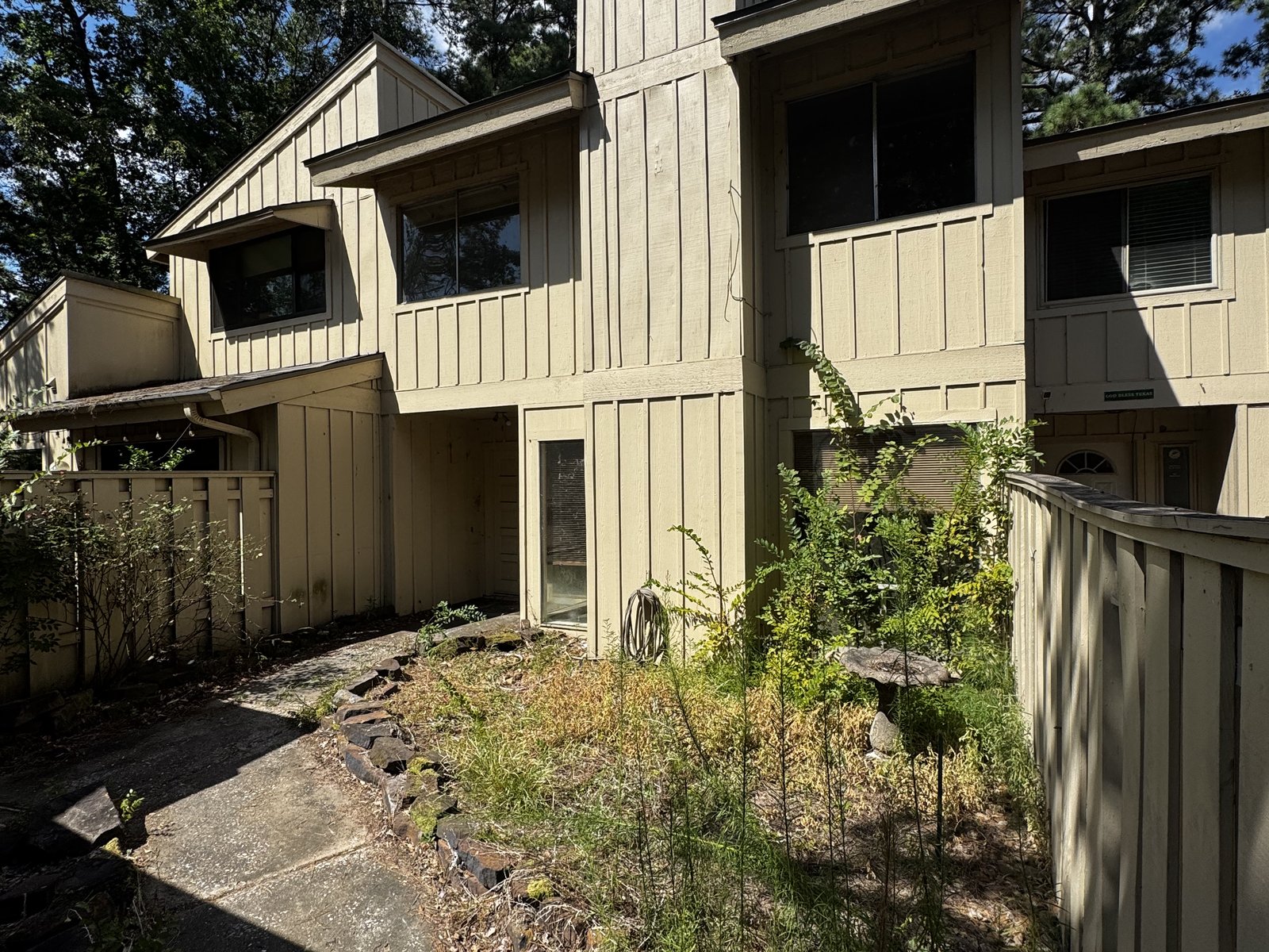 Overgrown exterior of an abandoned inherited townhome in Grogan's Mill, The Woodlands, TX