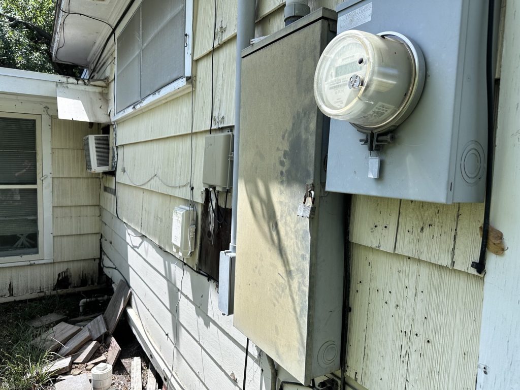 Weathered service equipment and rotted siding on as-is home bought in Freeport TX