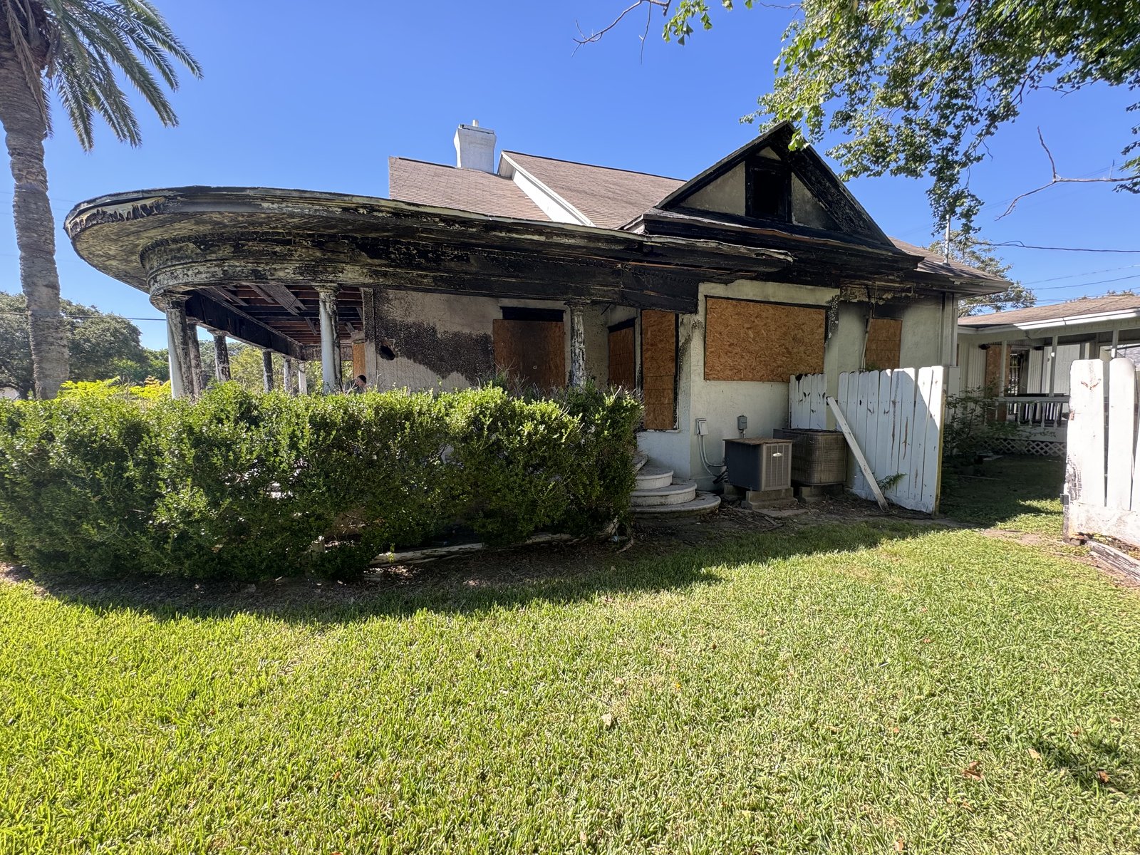Fire-damaged front porch and boarded windows of as-is home bought for cash in Texas City TX
