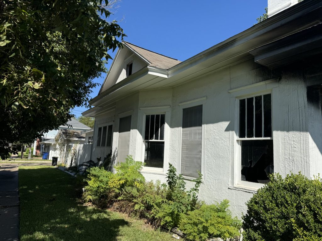 Scorched eaves and broken window on fire-damaged home purchased as-is in Texas City TX