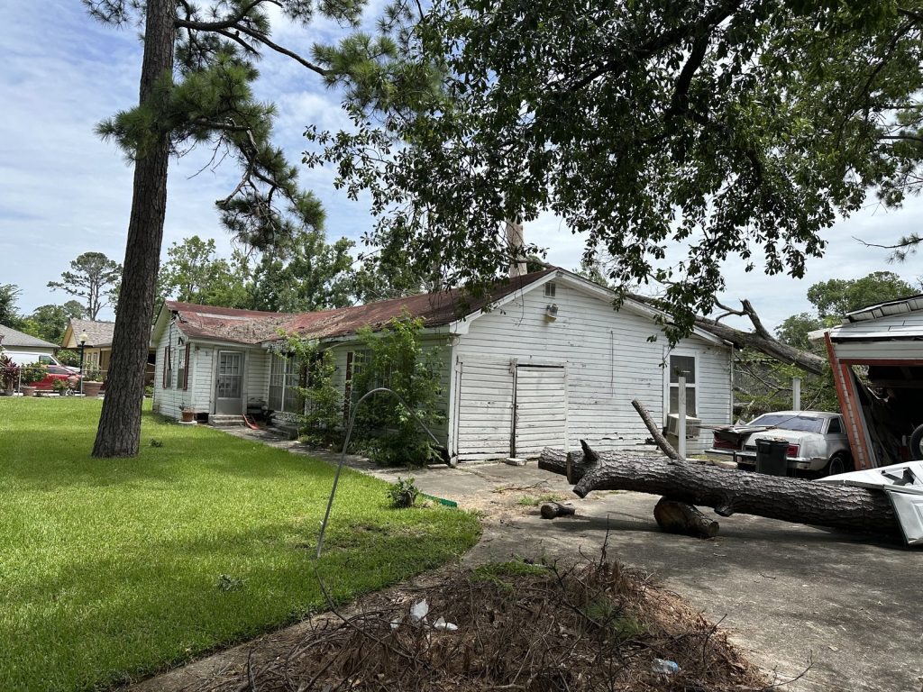 Storm-damaged roofline with a fallen tree limb on a hoarder house in Houston Gardens, Houston TX bought for cash