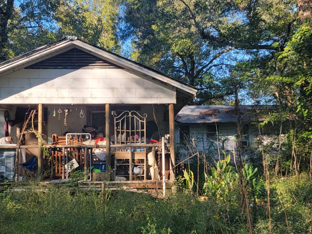 Cluttered front porch of a distressed rural property sold for cash in Cleveland, TX