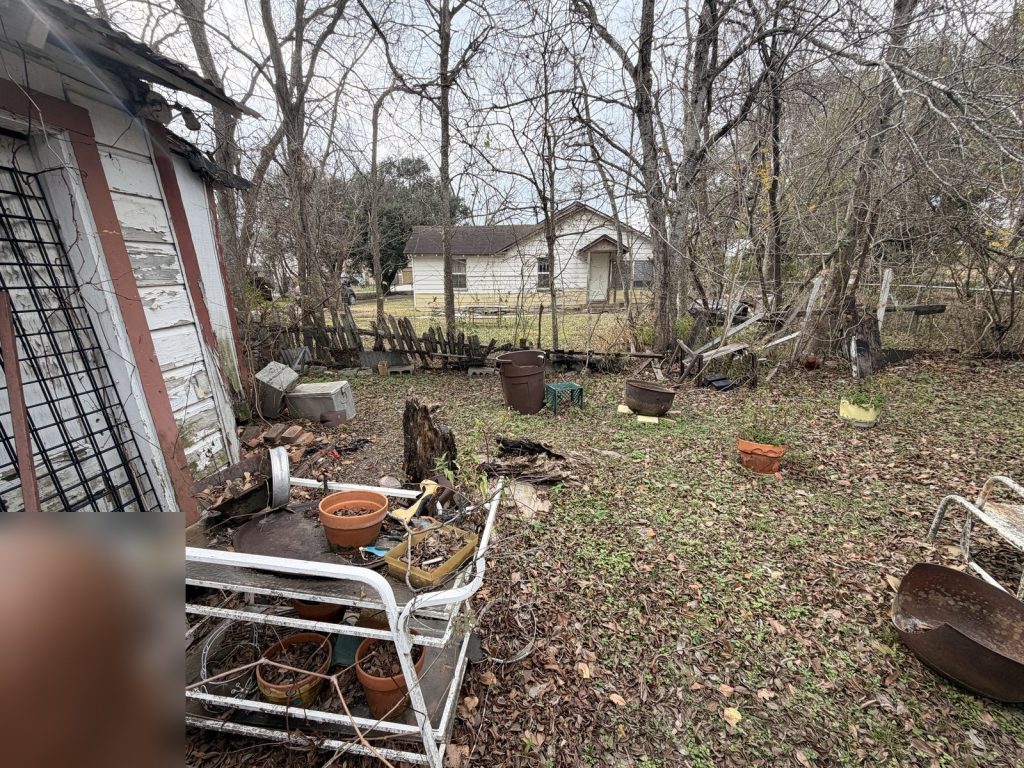 Cluttered backyard and outbuilding of estate home bought as-is in Houston TX