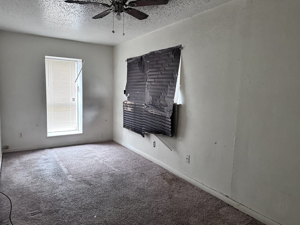 Storm-damaged window covered with plastic inside an Inwood Estates, Houston home sold as-is
