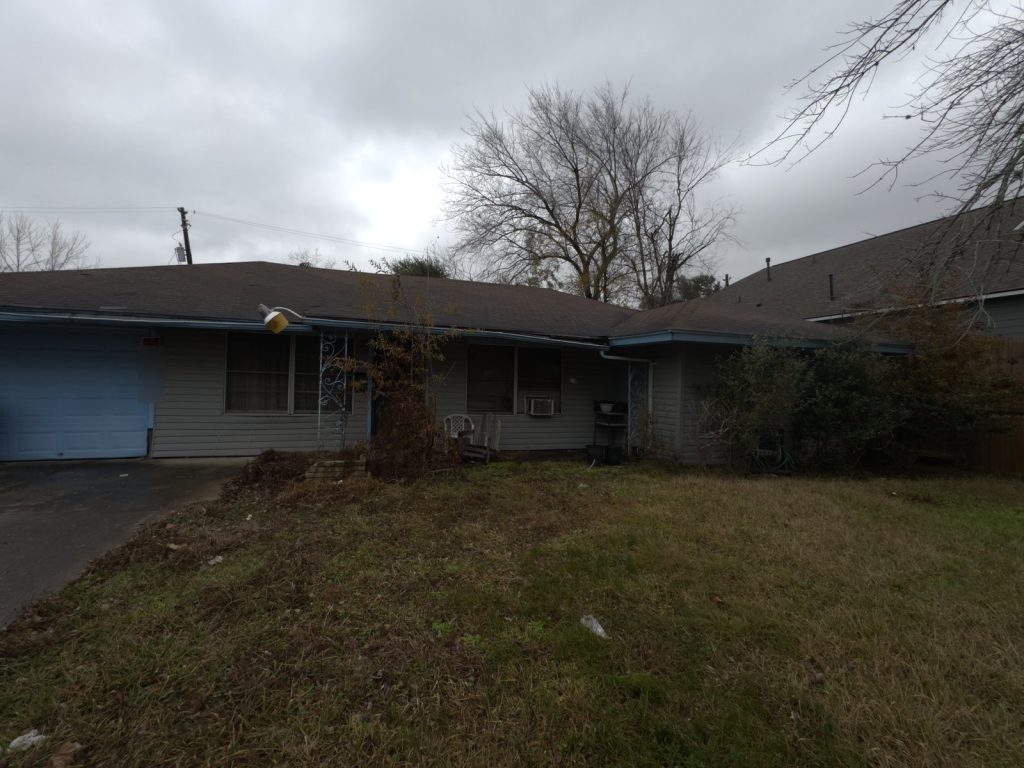 Exterior of as-is ranch home with overgrown yard purchased in Houston TX