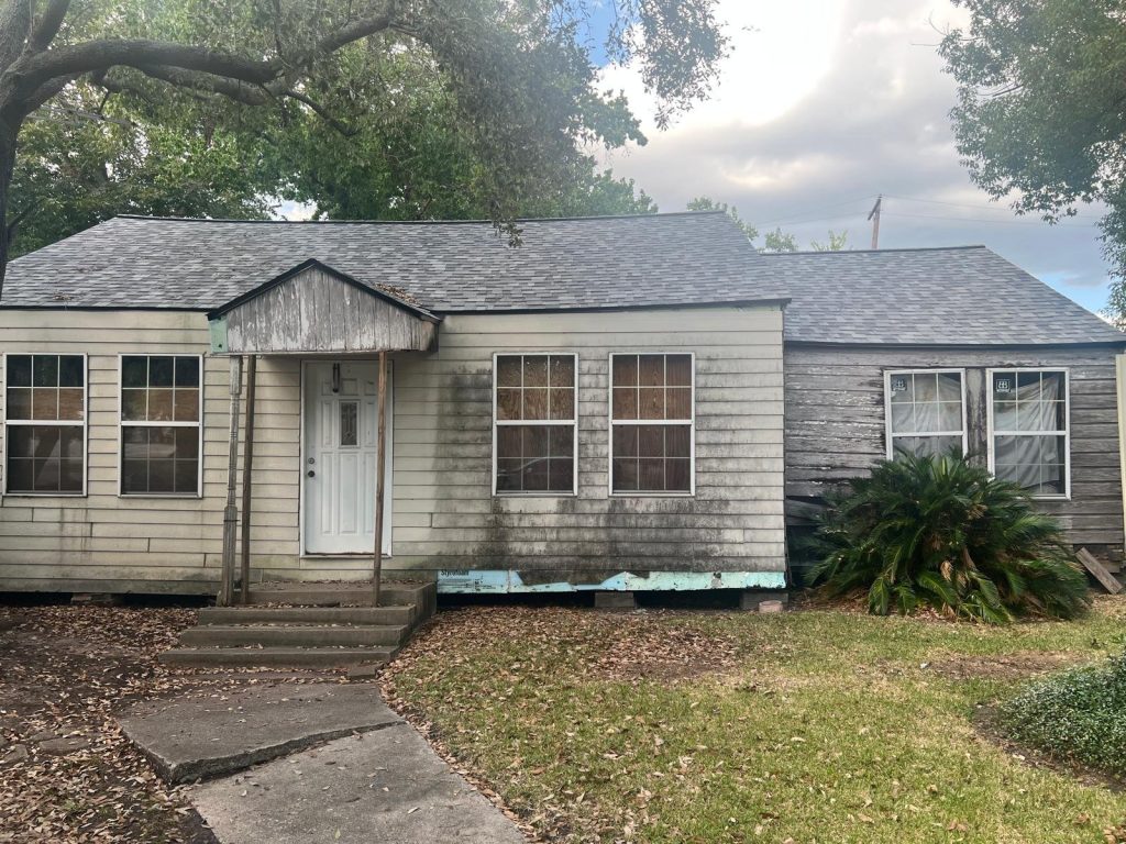 Front of severely weathered home with boarded windows bought for cash as-is in Baytown TX
