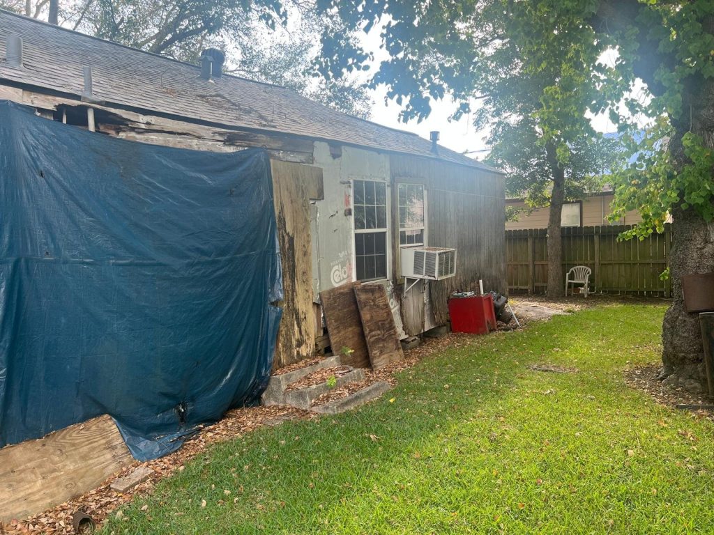 Rear exterior with tarp roof repair and rotted siding on distressed Baytown TX home purchased for cash