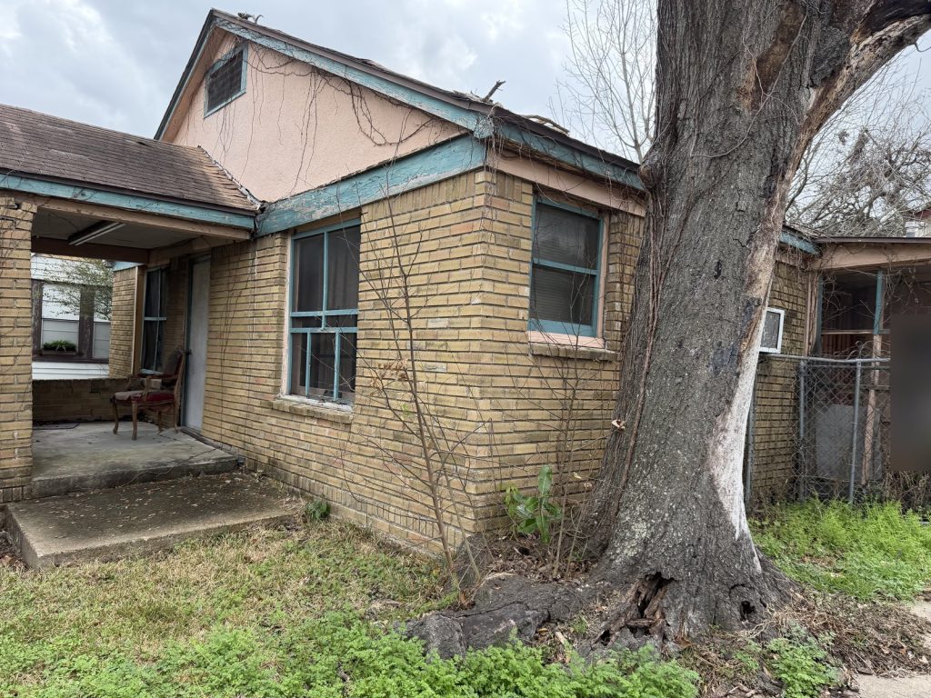 Vine-covered eaves and roof damage on vacant Houston TX home sold as-is