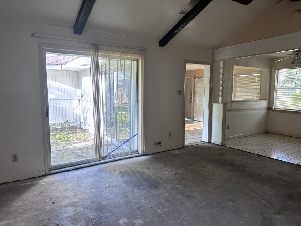 Empty living room with sliding door in a vandalized property sold for cash in High Meadows, Aldine, TX