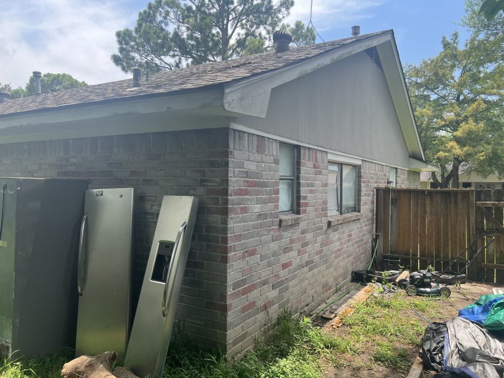 Side yard with discarded appliances at Houston TX rental bought by cash home buyers