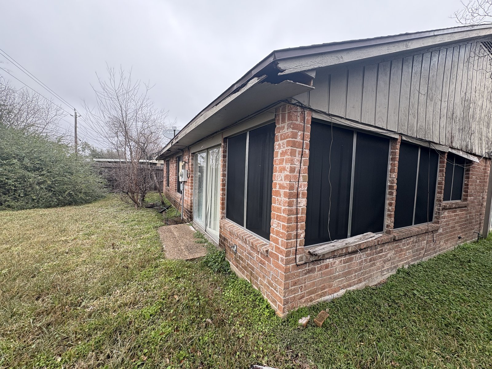 Side view of abandoned home with damaged fascia bought for cash in Woodland Trails, Houston TX